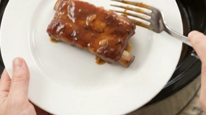 Slow cooker country-style pork ribs glazed with honey hickory BBQ sauce, topped with garlic cloves and rosemary