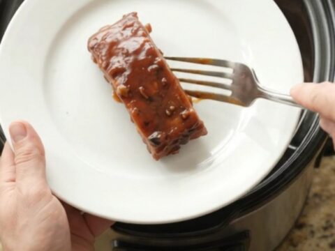 Slow cooker country pork ribs glazed in thick BBQ sauce, garnished with fresh herbs, on a white plate.