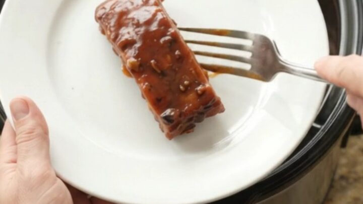 Slow cooker country pork ribs glazed in thick BBQ sauce, garnished with fresh herbs, on a white plate.