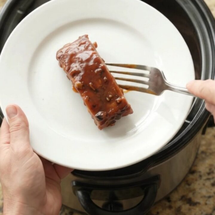 Slow cooker country pork ribs glazed in thick BBQ sauce, garnished with fresh herbs, on a white plate.