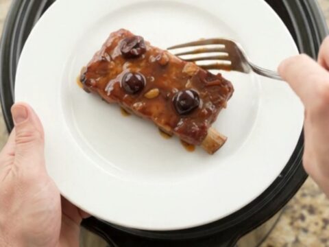 Slow cooker cherry cola BBQ ribs glistening with dark sauce and cherries