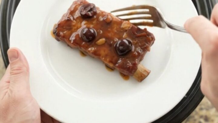 Slow cooker cherry cola BBQ ribs glistening with dark sauce and cherries