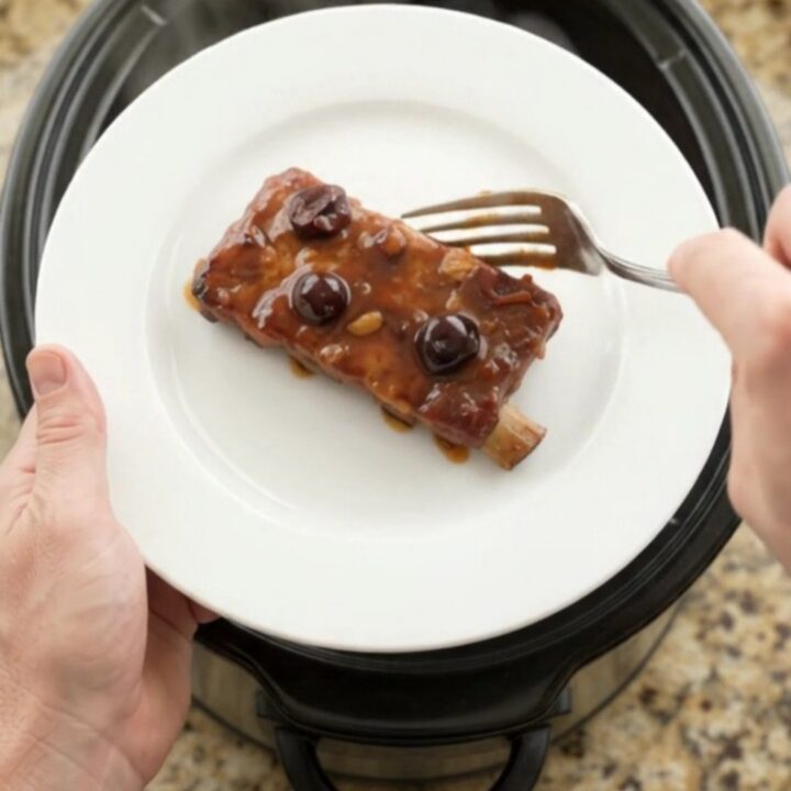 Slow cooker cherry cola BBQ ribs glistening with dark sauce and cherries