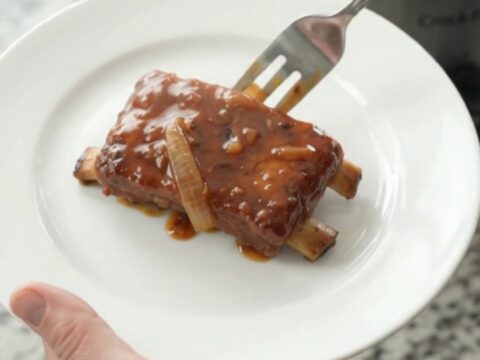 Slow cooker full of glazed pork ribs with caramelized onions and BBQ sauce