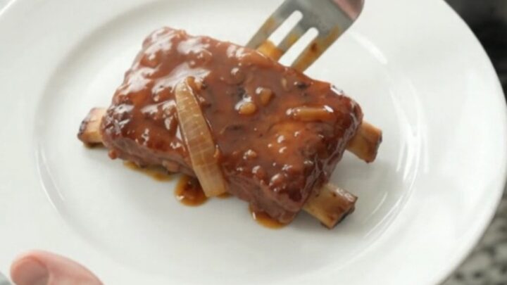 Slow cooker full of glazed pork ribs with caramelized onions and BBQ sauce