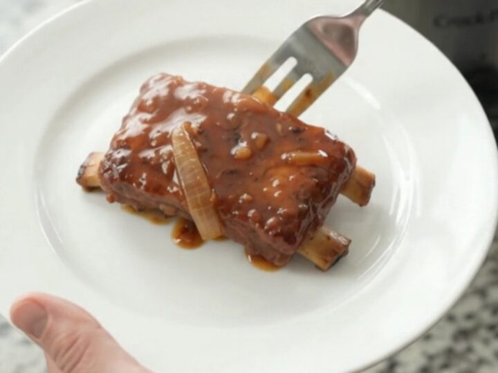 Slow cooker full of glazed pork ribs with caramelized onions and BBQ sauce