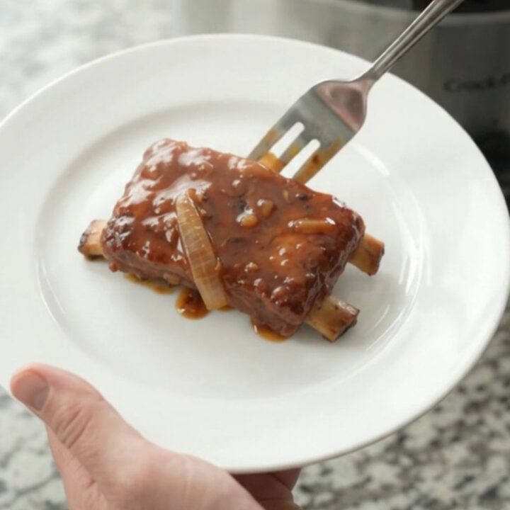 Slow cooker full of glazed pork ribs with caramelized onions and BBQ sauce