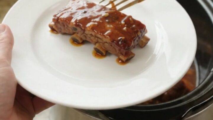 Slow-cooker garlic herb BBQ country ribs in a black ceramic pot with sauce and rosemary