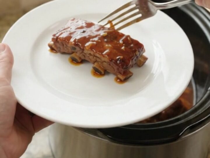 Slow-cooker garlic herb BBQ country ribs in a black ceramic pot with sauce and rosemary