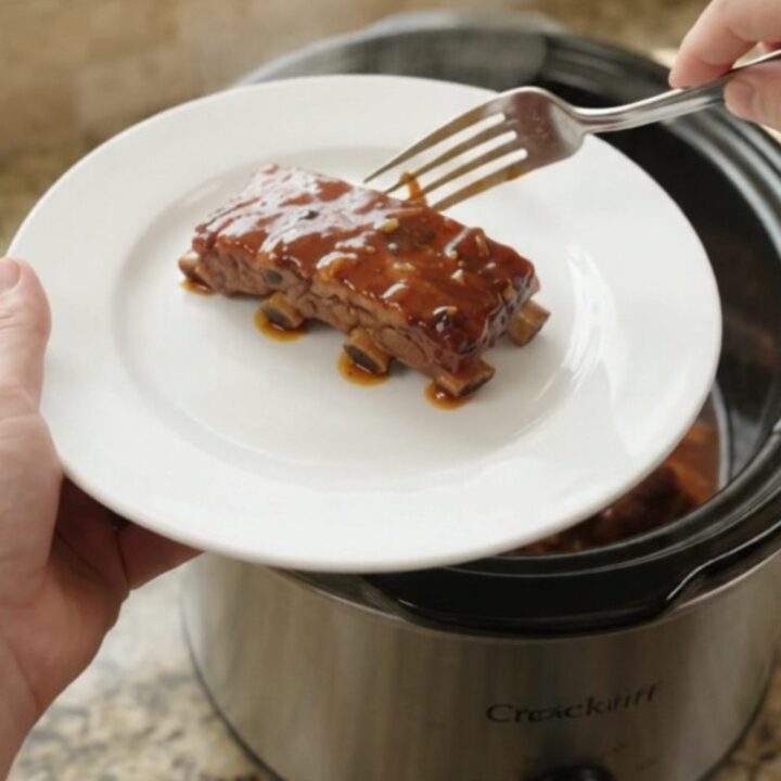 Slow-cooker garlic herb BBQ country ribs in a black ceramic pot with sauce and rosemary
