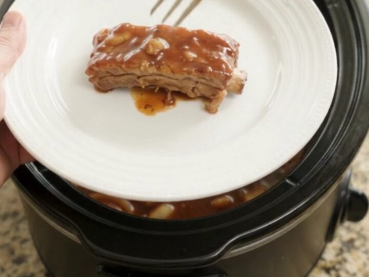 Root beer BBQ country ribs in a slow cooker, glazed with dark sauce and topped with caramelized onions.