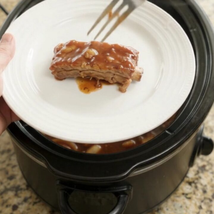 Root beer BBQ country ribs in a slow cooker, glazed with dark sauce and topped with caramelized onions.