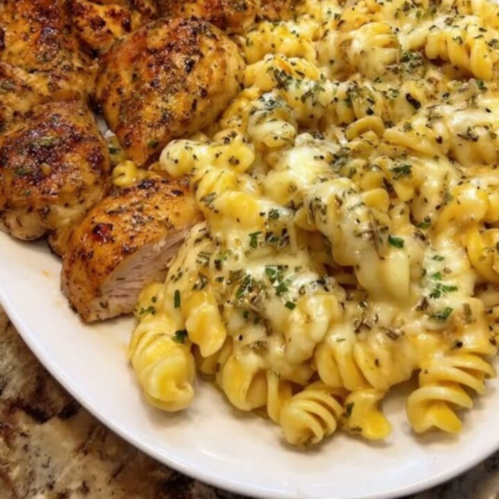 A close-up of creamy parmesan rotini with pieces of golden garlic butter chicken in a bowl.