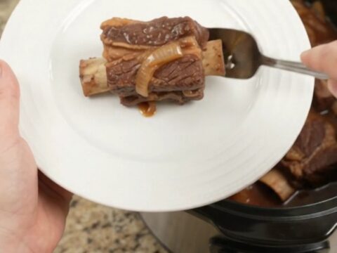 Brown Sugar BBQ Short Ribs in a slow cooker, glistening with sticky barbecue sauce and caramelized onions.