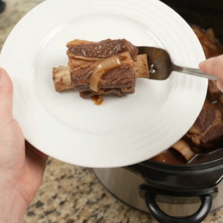 Brown Sugar BBQ Short Ribs in a slow cooker, glistening with sticky barbecue sauce and caramelized onions.