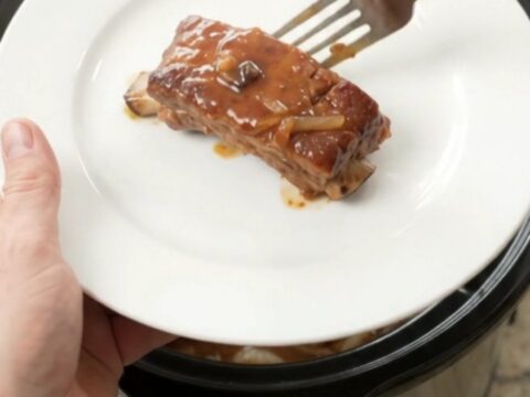 Tender pork ribs glazed with maple bourbon barbecue sauce, topped with caramelized onions in a slow cooker.