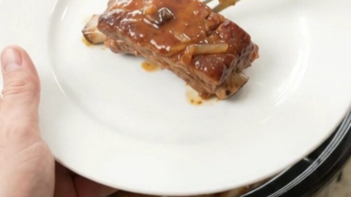 Tender pork ribs glazed with maple bourbon barbecue sauce, topped with caramelized onions in a slow cooker.