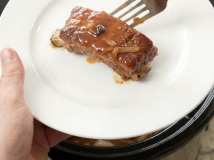Tender pork ribs glazed with maple bourbon barbecue sauce, topped with caramelized onions in a slow cooker.