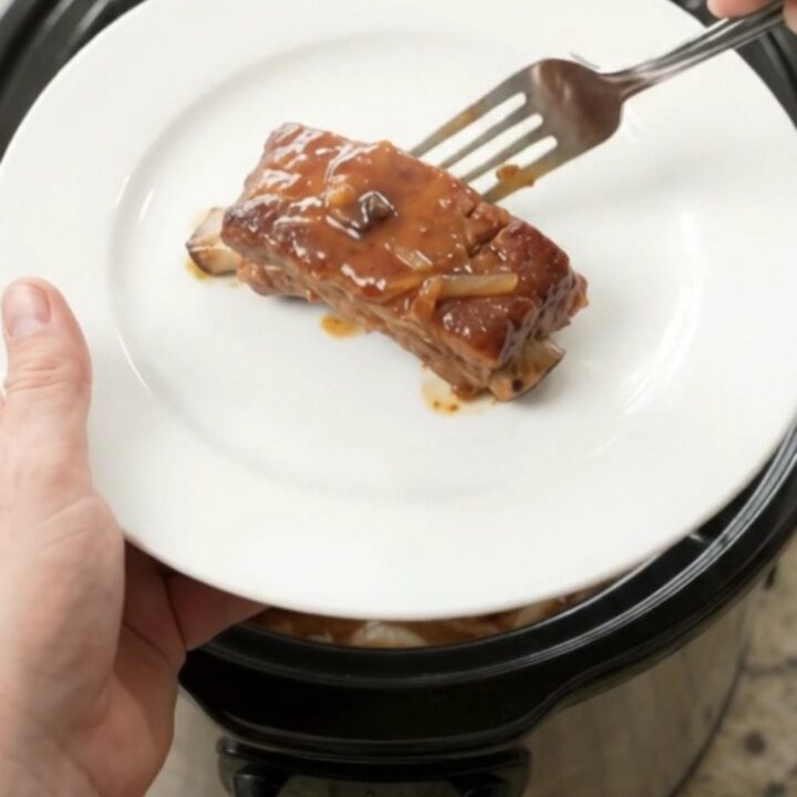 Tender pork ribs glazed with maple bourbon barbecue sauce, topped with caramelized onions in a slow cooker.