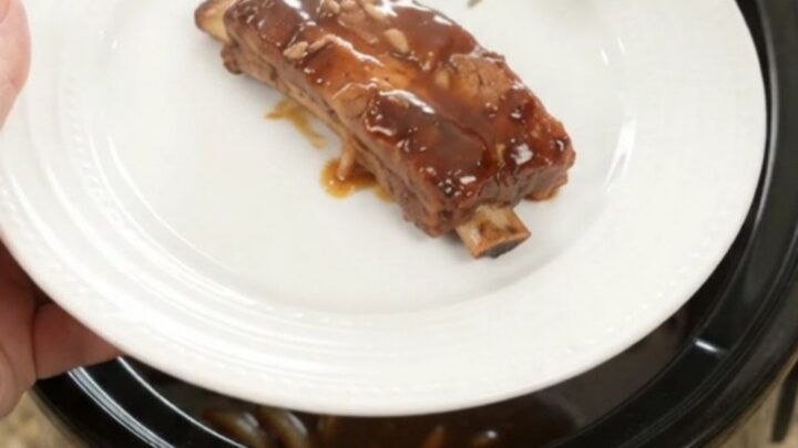Slow cooker full of glazed root beer molasses pork ribs with caramelized onions