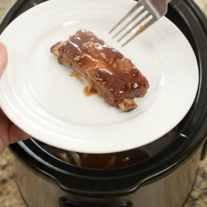 Slow cooker full of glazed root beer molasses pork ribs with caramelized onions