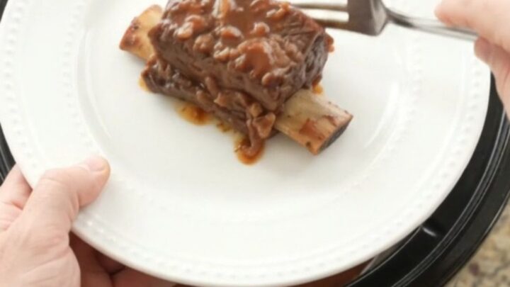 Slow cooker beef short ribs in a glossy dark sauce with apples, ready to serve