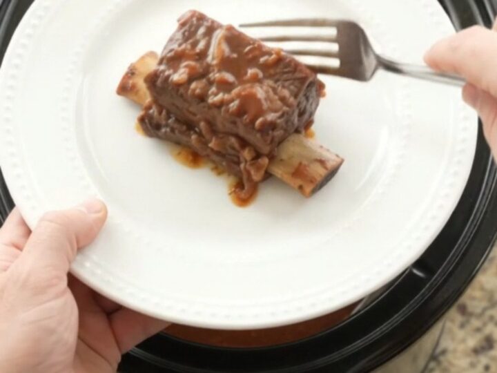 Slow cooker beef short ribs in a glossy dark sauce with apples, ready to serve