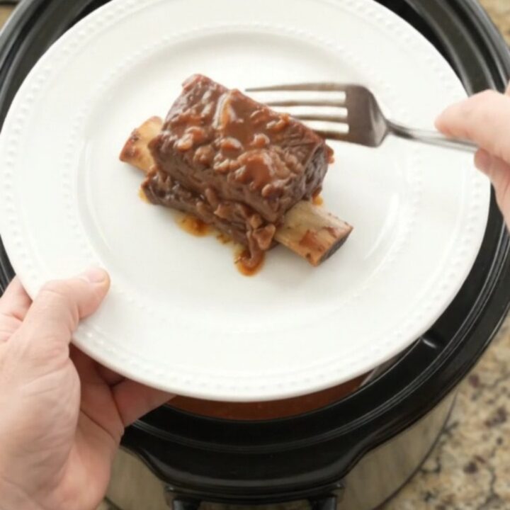Slow cooker beef short ribs in a glossy dark sauce with apples, ready to serve