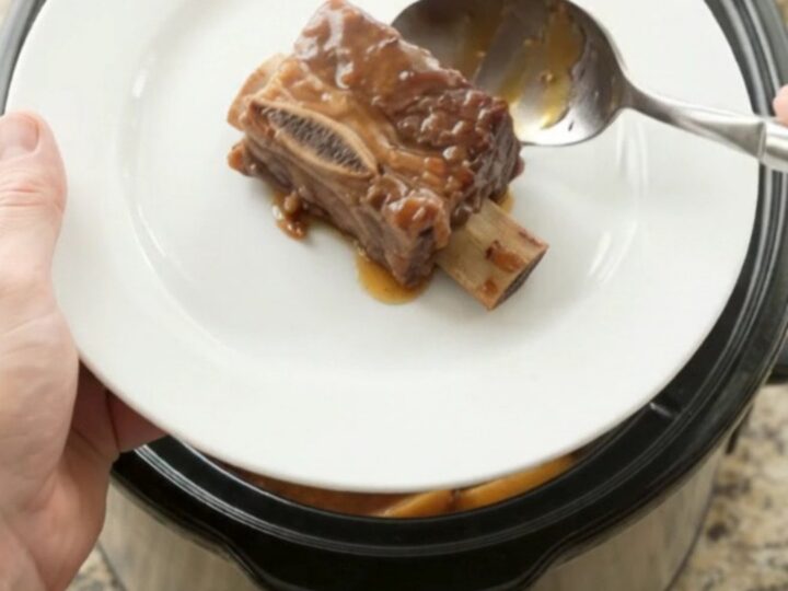 Tender beef short ribs in a crockpot with apples and BBQ sauce, steam rising