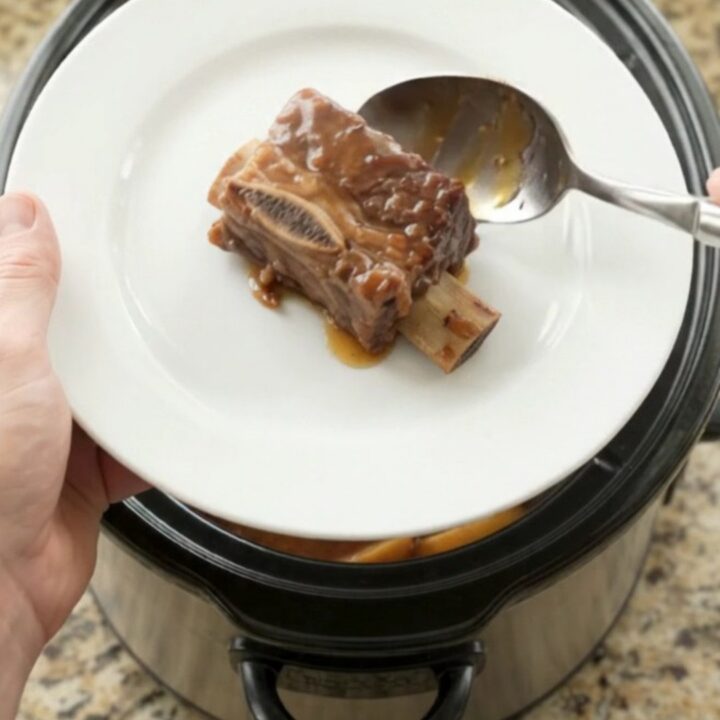 Tender beef short ribs in a crockpot with apples and BBQ sauce, steam rising