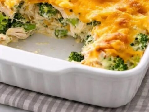 A steaming serving of cheesy chicken divan casserole being lifted from a white baking dish with a spatula.