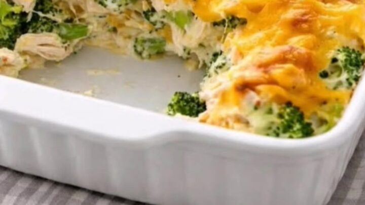 A steaming serving of cheesy chicken divan casserole being lifted from a white baking dish with a spatula.