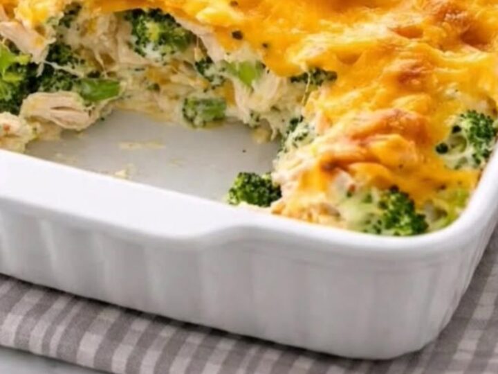 A steaming serving of cheesy chicken divan casserole being lifted from a white baking dish with a spatula.