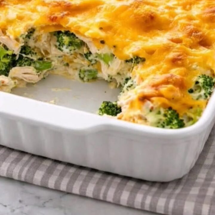 A steaming serving of cheesy chicken divan casserole being lifted from a white baking dish with a spatula.