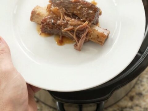 Slow-cooker beef short ribs glazed with honey hickory BBQ sauce and pineapple rings on a white plate.