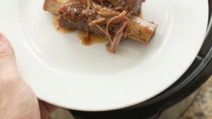 Slow-cooker beef short ribs glazed with honey hickory BBQ sauce and pineapple rings on a white plate.