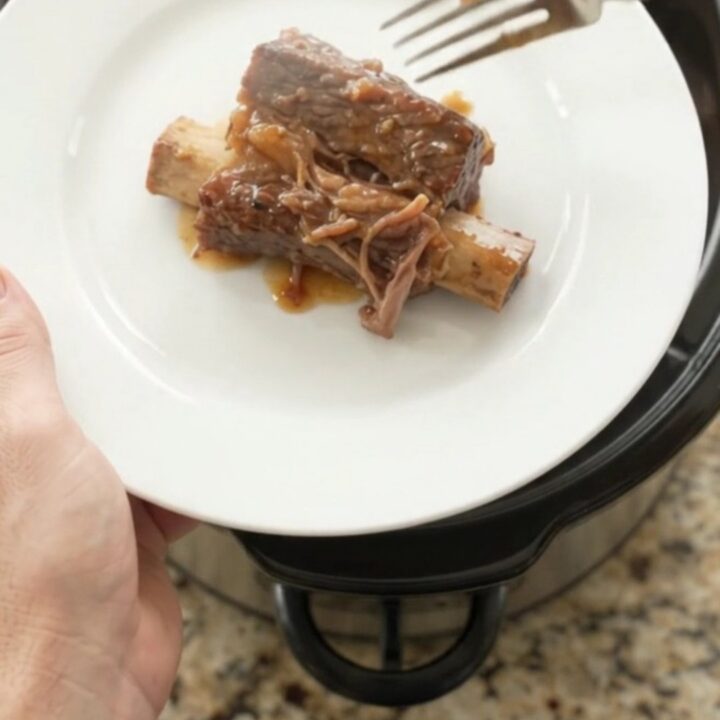 Slow-cooker beef short ribs glazed with honey hickory BBQ sauce and pineapple rings on a white plate.