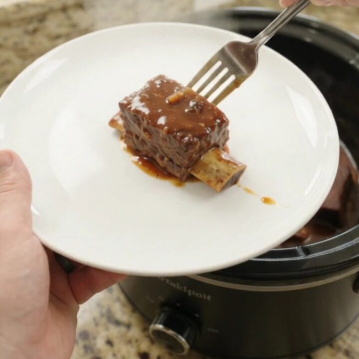 Slow cooker full of glazed beef short ribs in barbecue sauce with chipotle peppers