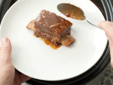 Bourbon peach BBQ short ribs in a crockpot, glistening with sauce and topped with soft peach slices.