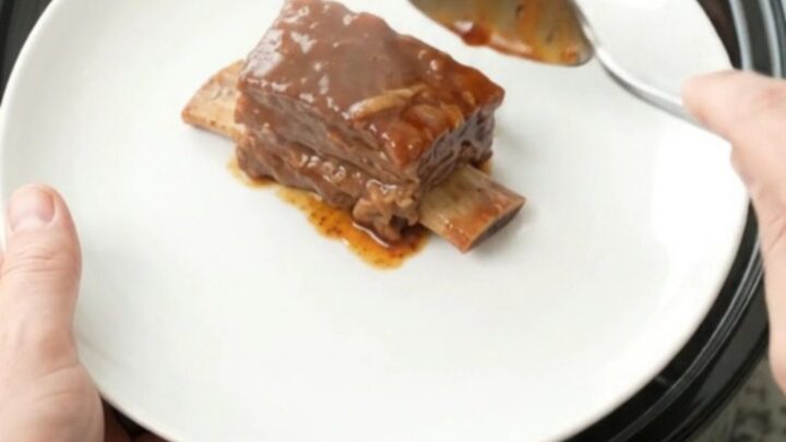 Bourbon peach BBQ short ribs in a crockpot, glistening with sauce and topped with soft peach slices.