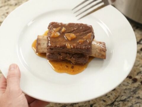 Slow-cooker beef short ribs glazed with peach bourbon BBQ sauce, garnished with soft peach slices.