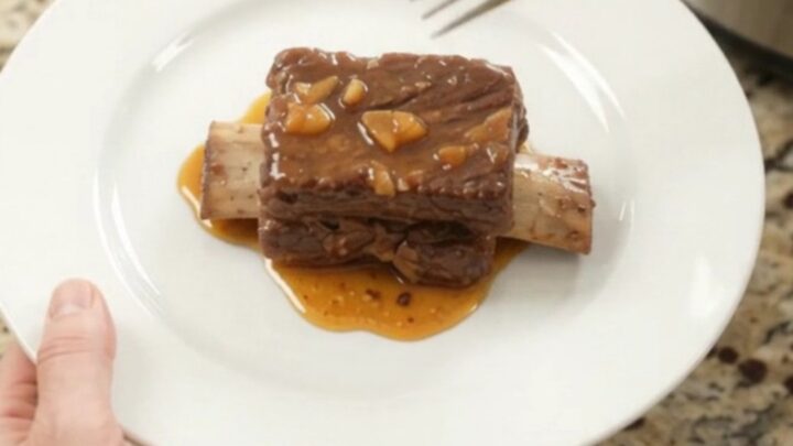 Slow-cooker beef short ribs glazed with peach bourbon BBQ sauce, garnished with soft peach slices.