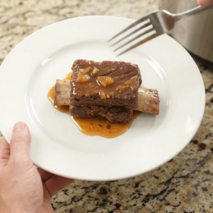 Slow-cooker beef short ribs glazed with peach bourbon BBQ sauce, garnished with soft peach slices.
