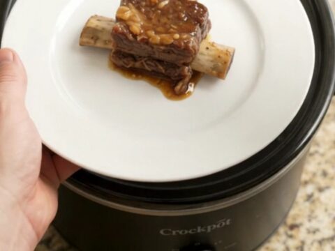 A slow cooker filled with glossy, tender beef short ribs and caramelized pineapple rings in a rich maple bourbon sauce.