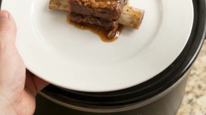 A slow cooker filled with glossy, tender beef short ribs and caramelized pineapple rings in a rich maple bourbon sauce.