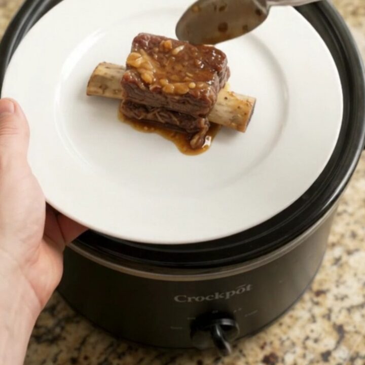 A slow cooker filled with glossy, tender beef short ribs and caramelized pineapple rings in a rich maple bourbon sauce.