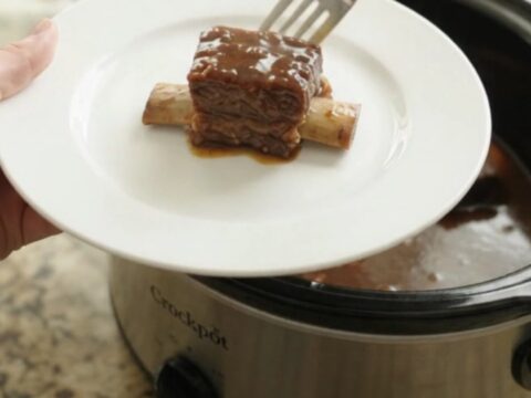 Bone-in beef short ribs glistening with molasses garlic sauce in a black slow cooker