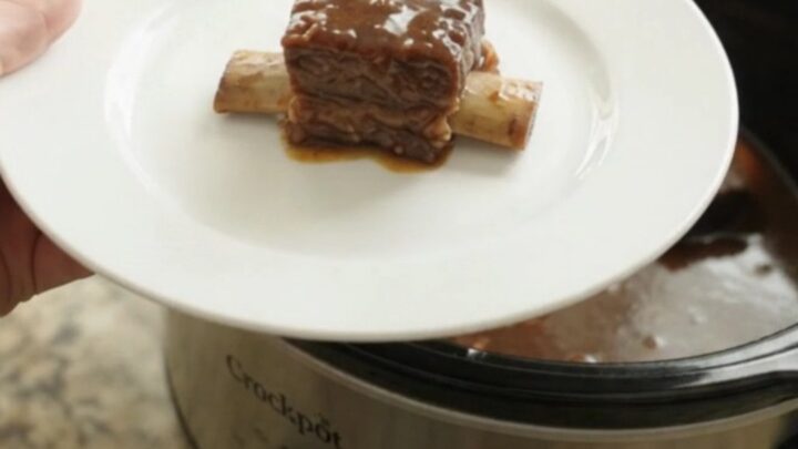 Bone-in beef short ribs glistening with molasses garlic sauce in a black slow cooker