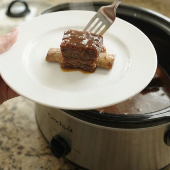 Bone-in beef short ribs glistening with molasses garlic sauce in a black slow cooker