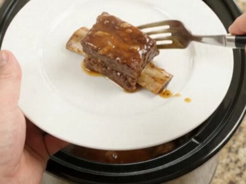 Slow cooker beef short ribs in a glossy chipotle honey barbecue sauce, garnished with fresh herbs.